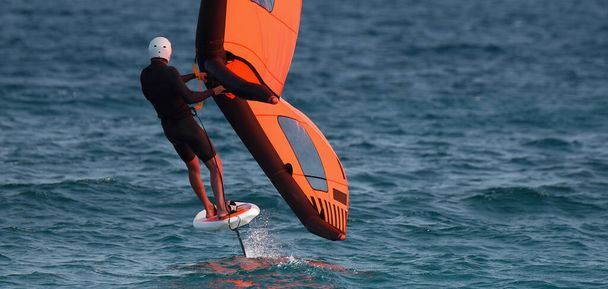 Человек летит на крыльях, используя надувные крылья и подводные доски для серфинга в голубом океане, ездит верхом на ветровом крыле, катается на волнах - Фото, изображение