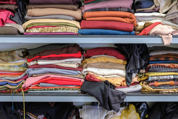 Multicolored various clothes stacked in piles on a shelf in a atelier - Photo, Image