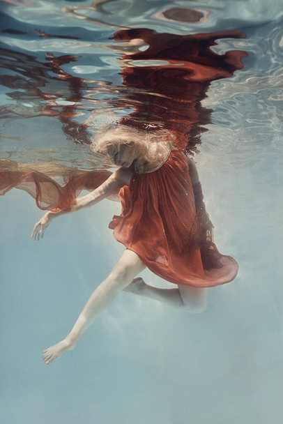     A woman in a dress swims underwater as if floating in zero gravity                            - 写真・画像