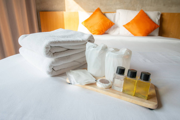 Hotellin mukavuudet (kuten pyyhkeet, shampoo, saippua, juomalasi jne.) sängyllä. Hotellin mukavuudet on jotain premium-luontoa, joka tarjotaan huoneen lisäksi huonetta vuokrattaessa. - Valokuva, kuva