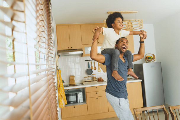 African American Father carrying his little boy playing in kitchen together indoor, Cheerful Black Brazilian Dad and son laughing piggyback at home. - Foto, Imagen