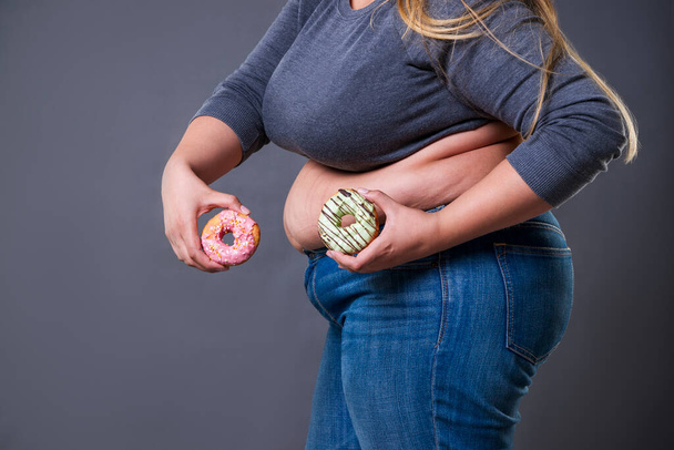 Fat woman posing with donuts on a gray background, fast food and unhealthy nutrition concept - Фото, зображення