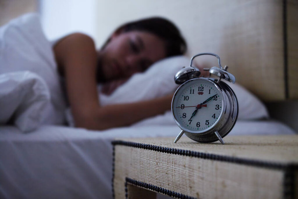 Den Tag verschlafen. Eine junge Frau schläft mit ihrem Wecker neben ihrem Bett. - Foto, Bild