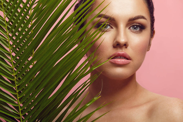 studio beauty portrait of beautiful caucasian brunette woman with branch of palm on pink isolated  - Fotografie, Obrázek