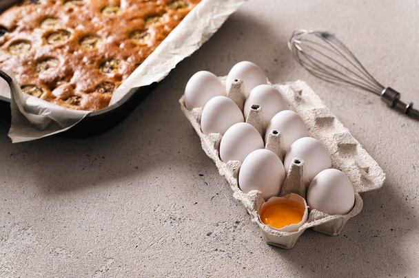 Chicken white eggs in a pan on a light background, one egg is broken and seen yolk, baked cake on the far plan, rear side light - Foto, immagini