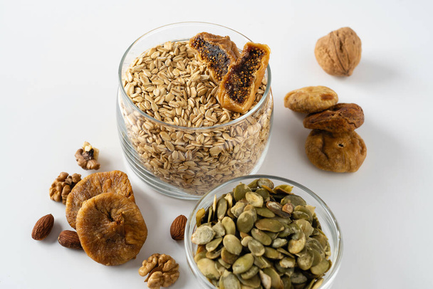 Výrobky pro zdravou snídani, rolované ovesné krupice se sušeným ovocem, ořechy a dýňovými semínky na bílém pozadí, detailní záběr - Fotografie, Obrázek