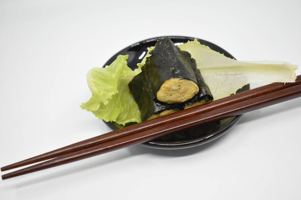 Sushi avec feuilles nori et houmous de pois chiches avec laitue sur une assiette noire et baguettes en bois. Fond gris clair. - Photo, image