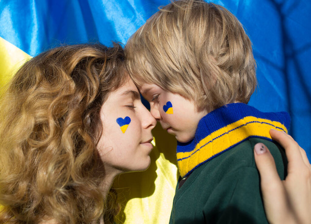 Обличчя хлопчика і молодої жінки з пофарбованим жовто - синім серцем на щоках. Сім'я, єдність, підтримка. Українці проти війни. Благаю про допомогу для світової спільноти. Догляд один за одним. - Фото, зображення