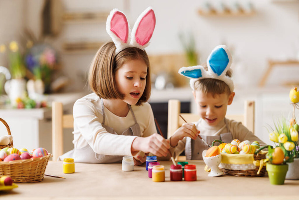 Curious kids brother and sister in bunny ears painting Easter eggs together in kitchen - Foto, Imagem