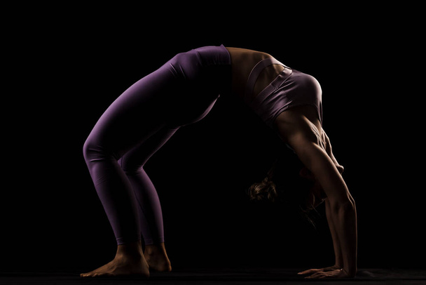 Fit girl practicing yoga in a studio. Half silhouette side lit fitness model - Photo, Image