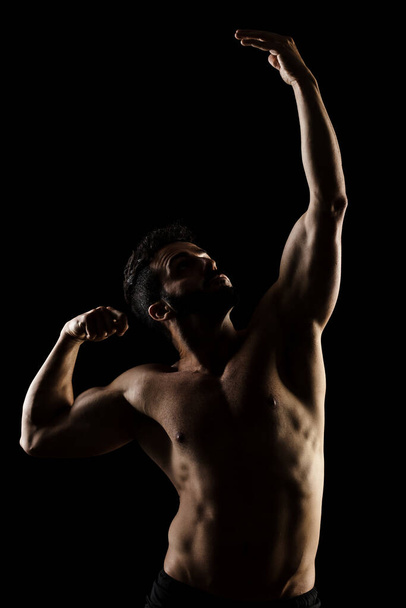 Side lit muscular Caucasian man silhouette. Athlete posing against black background.  - Fotó, kép