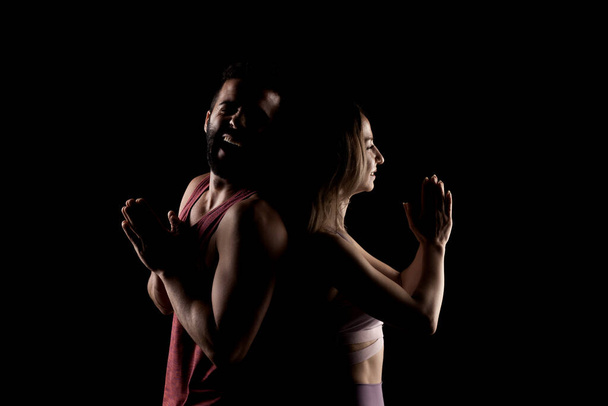 Fit couple posing together. Girl praying boy having fun. Side lit silhouettes on black background. - Foto, immagini