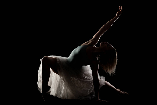 ballerina with a white dress and black top posing on black background. side lit silhouette - Фото, изображение
