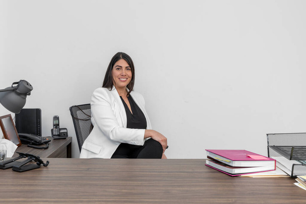 Mulher de negócios sentada em sua mesa enquanto olha para a câmera sorrindo. Executiva confiante em seu escritório. - Foto, Imagem