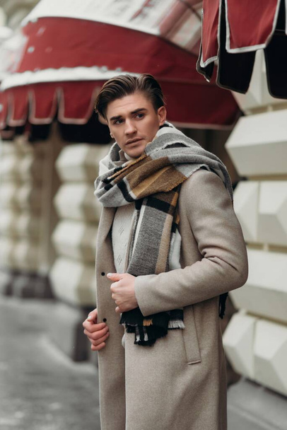 Νεαρός που φοράει παλτό και περπατάει στο δρόμο. Νεαρός γενειοφόρος με μοντέρνο χτένισμα στα αστικά - Φωτογραφία, εικόνα