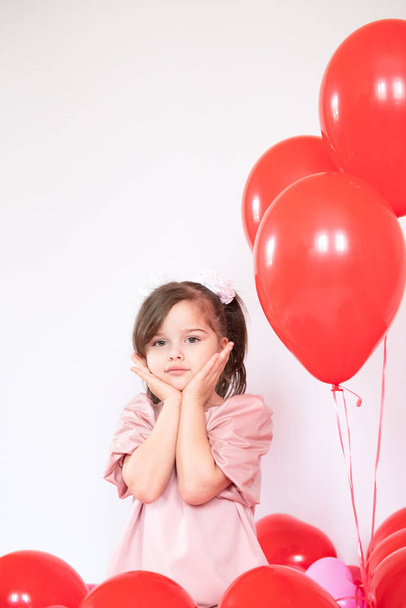 Cute little girl holding a bunch of red heart-shaped balloons - Фото, зображення