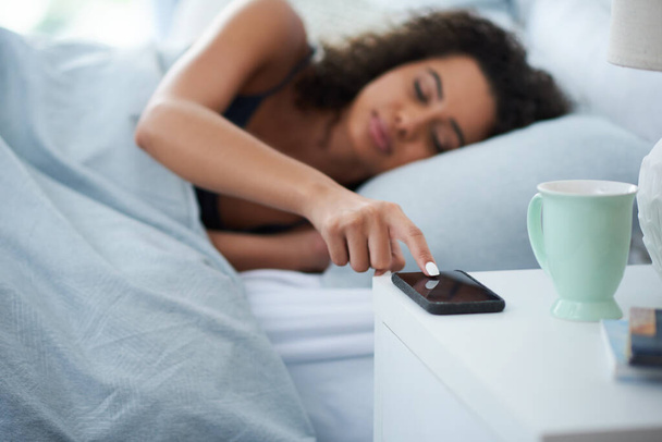 Nope, Im ignoring you Mr Alarm. Shot of an attractive young woman laying in bed during the morning and pressing snooze on her phone. - Foto, imagen