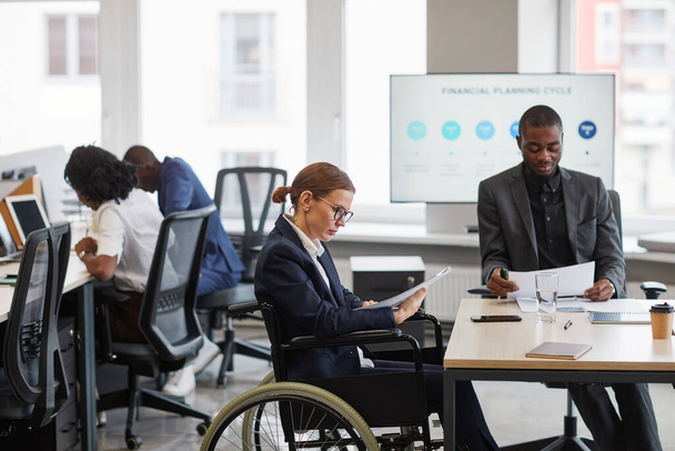 Portrait en grand angle d'une femme d'affaires utilisant un fauteuil roulant lors d'une réunion d'affaires au bureau et parlant sur smartphone, espace de copie - Photo, image