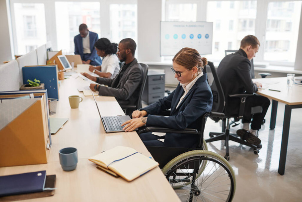 Вид сбоку портрет улыбающейся деловой женщины с инвалидной коляской во время работы с коллегой в офисе, копировальное пространство - Фото, изображение