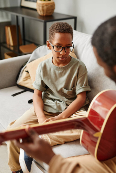 Vertical portrait of young African-American boy learning to play guitar at home with music tutor - Фото, зображення