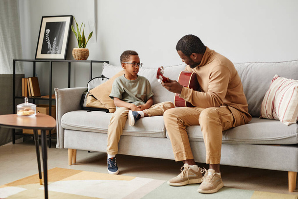 Full length portrait of African-American father teaching son to play guitar and musical instruments, copy space - Photo, Image