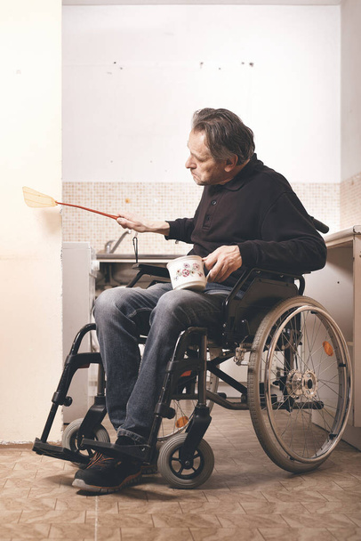 Old disabled man on wheel chair in his poor apartment - Fotó, kép