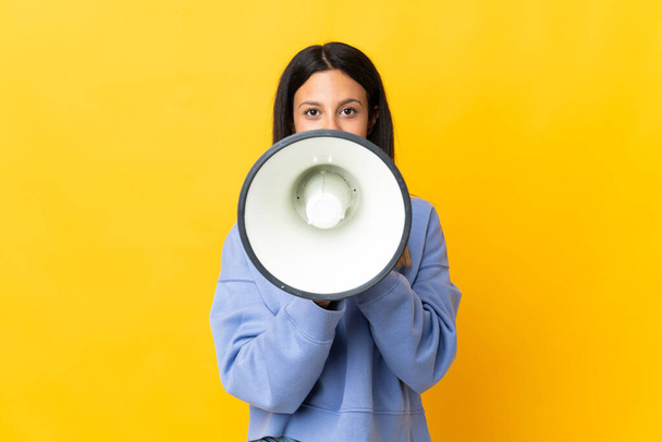 Caucasian girl isolated on yellow background shouting through a megaphone to announce something - Foto, Bild