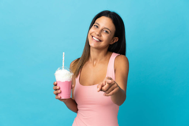 Νεαρή γυναίκα με μιλκσέικ φράουλα που δείχνει μπροστά με χαρούμενη έκφραση - Φωτογραφία, εικόνα