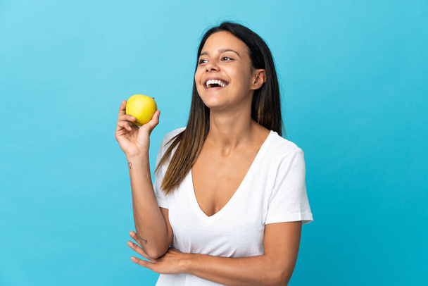 Menina caucasiana isolado no fundo azul com uma maçã e feliz - Foto, Imagem