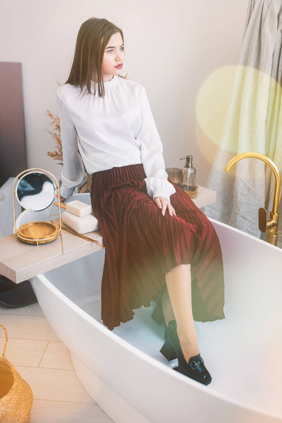 Portrait of fashionable women in red skirt, white blouse and stylish beige high-heeled shoes with a chain buckle posing in a bed - Foto, afbeelding