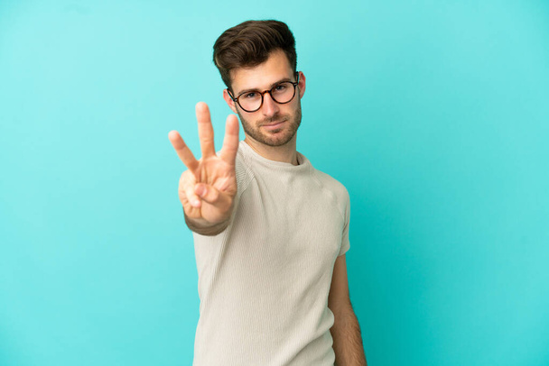 Junge kaukasische schöner Mann isoliert auf blauem Hintergrund glücklich und zählen drei mit den Fingern - Foto, Bild