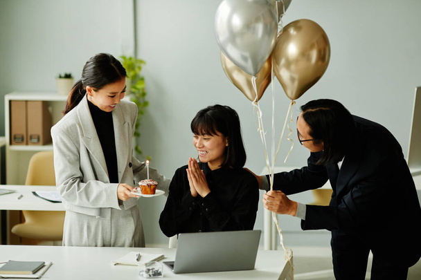 Portrait of colleagues bringing Birthday cake and balloons surprising smiling Asian woman in office - Zdjęcie, obraz
