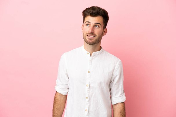 Young caucasian handsome man isolated on pink background thinking an idea while looking up - Fotó, kép