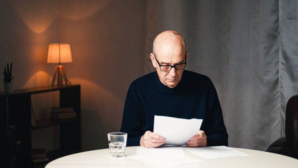 Elderly man sitting at the table reads his electricity and gas bills  - Photo, Image
