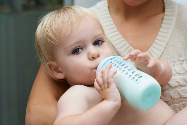 En sécurité dans les bras de sa mère. Un petit garçon buvant du lait de sa bouteille tout en étant tenu par sa mère. - Photo, image