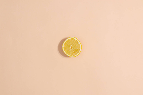 One sliced lemon on pastel beige background. Minimal flat lay summer fruits - Valokuva, kuva
