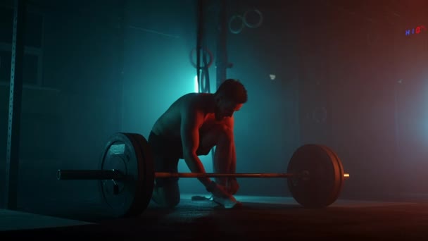 Güçlü atlet karanlık spor salonunda halteri kaldırmaya hazırlanıyor. Profesyonel sporcu salonda antrenman yapıyor. - Video, Çekim