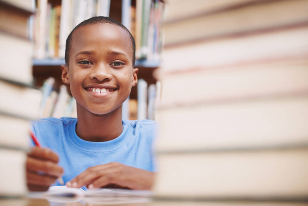 彼は本を打つのが好きだ。図書館の本に囲まれたアフリカ系アメリカ人の少年. - 写真・画像