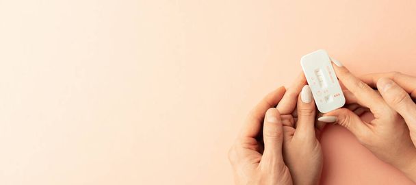 Kit de pruebas de embarazo. La mano femenina sostiene la prueba de embarazo positiva con cinta de seda sobre fondo rosa. Salud médica ginecológica, embarazo fertilidad maternidad personas concepto - Foto, Imagen