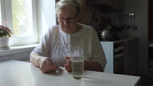 Een oudere vrouw neemt tablet en drinkt een glas water - Video