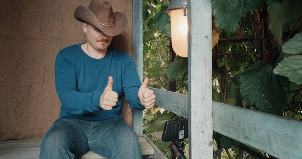 Cowboy man communicates online using his phone while sitting on porch - Photo, Image