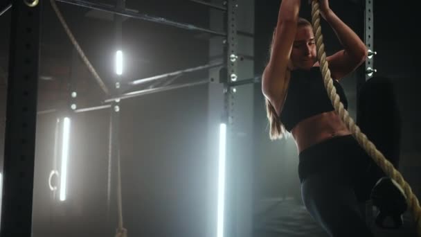 Спортивная молодая женщина в черной спортивной одежде прыгает по веревке и висит в спортзале - Кадры, видео