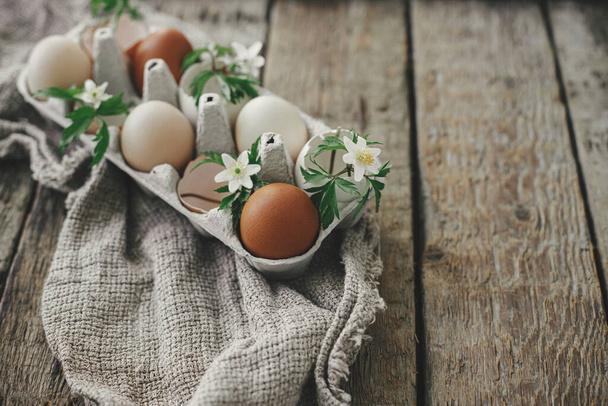 Великоднє сільське натюрморт. Натуральні великодні яйця з квітучими весняними квітами в лотку на сільському дерев'яному столі. З Великоднем! Проста стильна святкова прикраса на столі. Простір для тексту
 - Фото, зображення