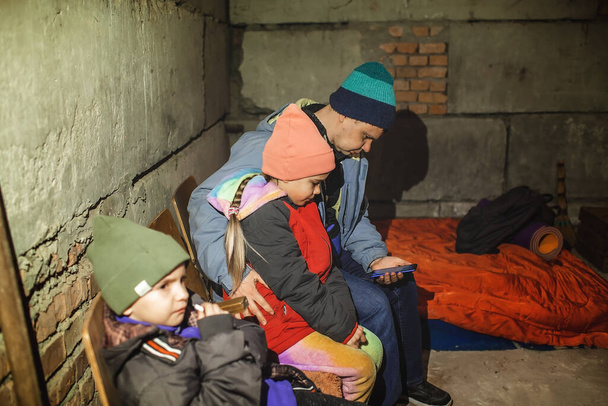 Pai ucraniano com crianças senta-se no abrigo anti-bomba e lê as últimas notícias de travagem sobre invasores russos - Foto, Imagem
