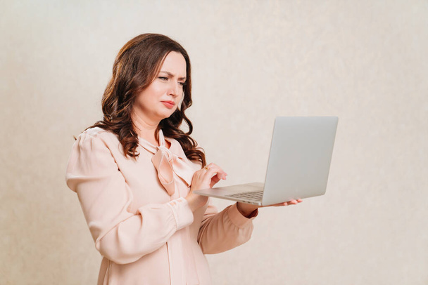 a puzzled woman in a beige dress with a laptop. online training and work. - Foto, imagen