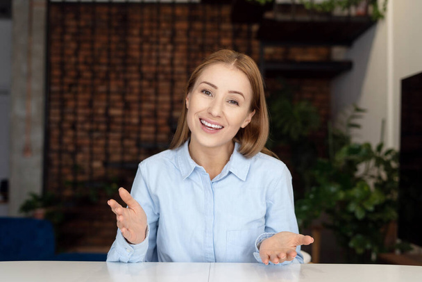 Portrait of smiling and gesturing woman looking at camera. Remote job concept. Company staff representative working in home office. Comfortable environment - Fotoğraf, Görsel