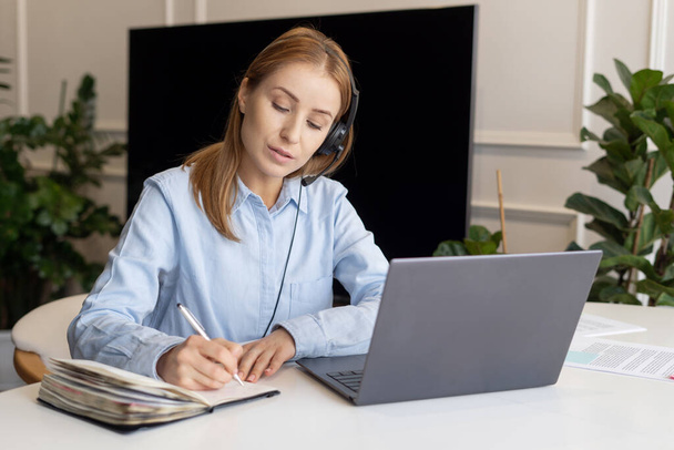 Portrait of woman using laptop and headset. Call center operator working from home. Remote work. Customer support worker deals with customer orders - Valokuva, kuva