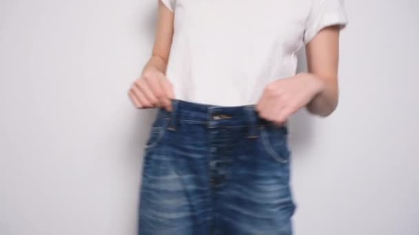 Happy woman dancing in oversized jeans on white background. The concept of diet, proper nutrition, weight loss and body positive. Slim Woman Showing Loose Jeans and her Loss Weight - Footage, Video