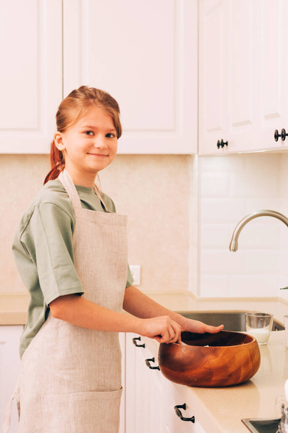 Mutfak önlüklü tatlı genç kız hamur pişirmek için ürünleri hazırlıyor ve yoğuruyor. - Fotoğraf, Görsel
