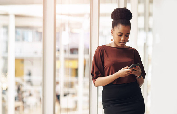 Staying connected is easy. Cropped shot of an attractive young businesswoman using her cellphone while standing in the office. - Photo, image